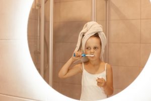 jolie-petite-fille-se-brosser-dents-dans-salle-bain-se-tenant-devant-miroir-vetue-t-shirt-blanc-sans-manches-enveloppe-ses-cheveux-dans-serviette-procedures-hygiene-du-matin